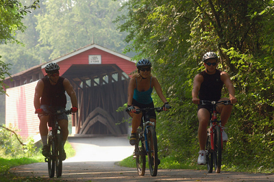 Three people biking on a train with a red covered bridge in the background.